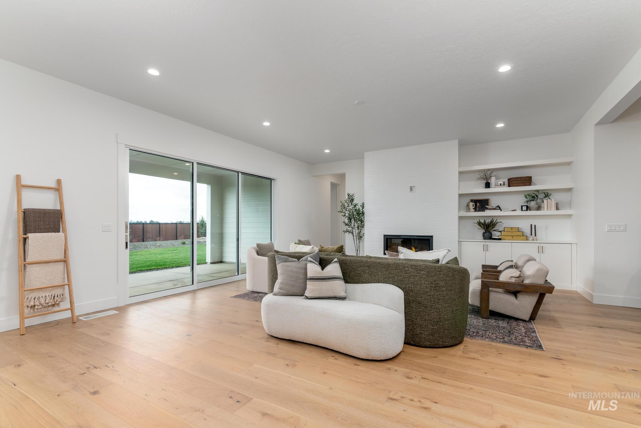 Spacious living area featuring light wood-finish flooring, recessed lighting, and a white fireplace