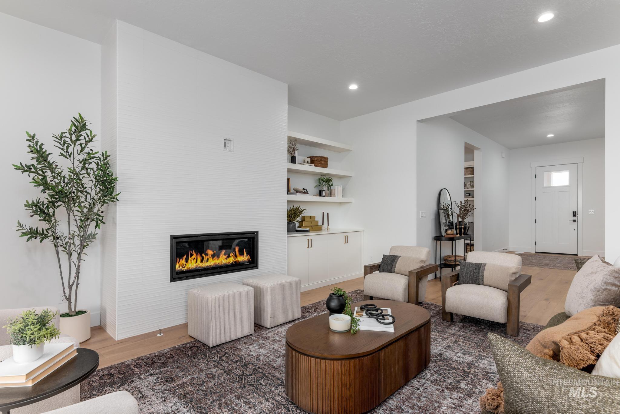 Living area featuring a linear electric fireplace with a white tile surround, built-in shelving, recessed lighting, and wood-finish flooring