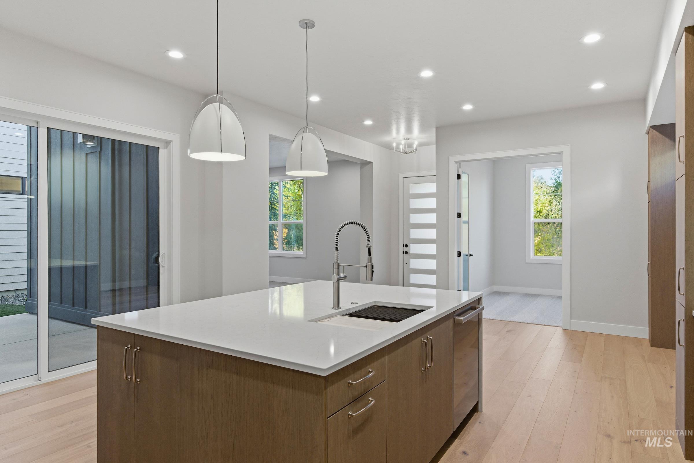 Kitchen with light wood finished floors, brown cabinetry, hanging light fixtures, recessed lighting, and modern cabinets