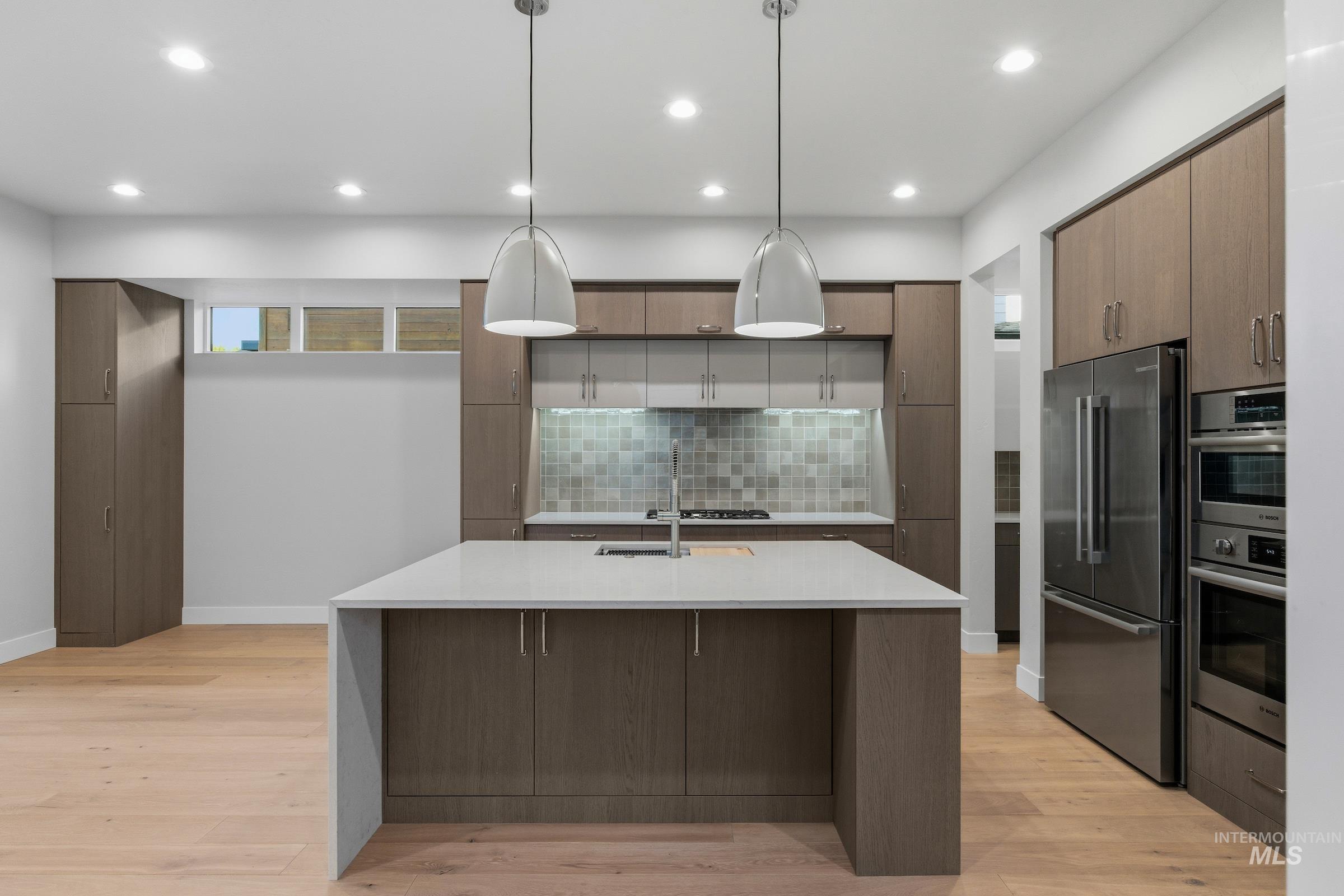 Kitchen featuring stainless steel appliances, pendant lighting, tasteful backsplash, modern cabinets, and light wood-style floors