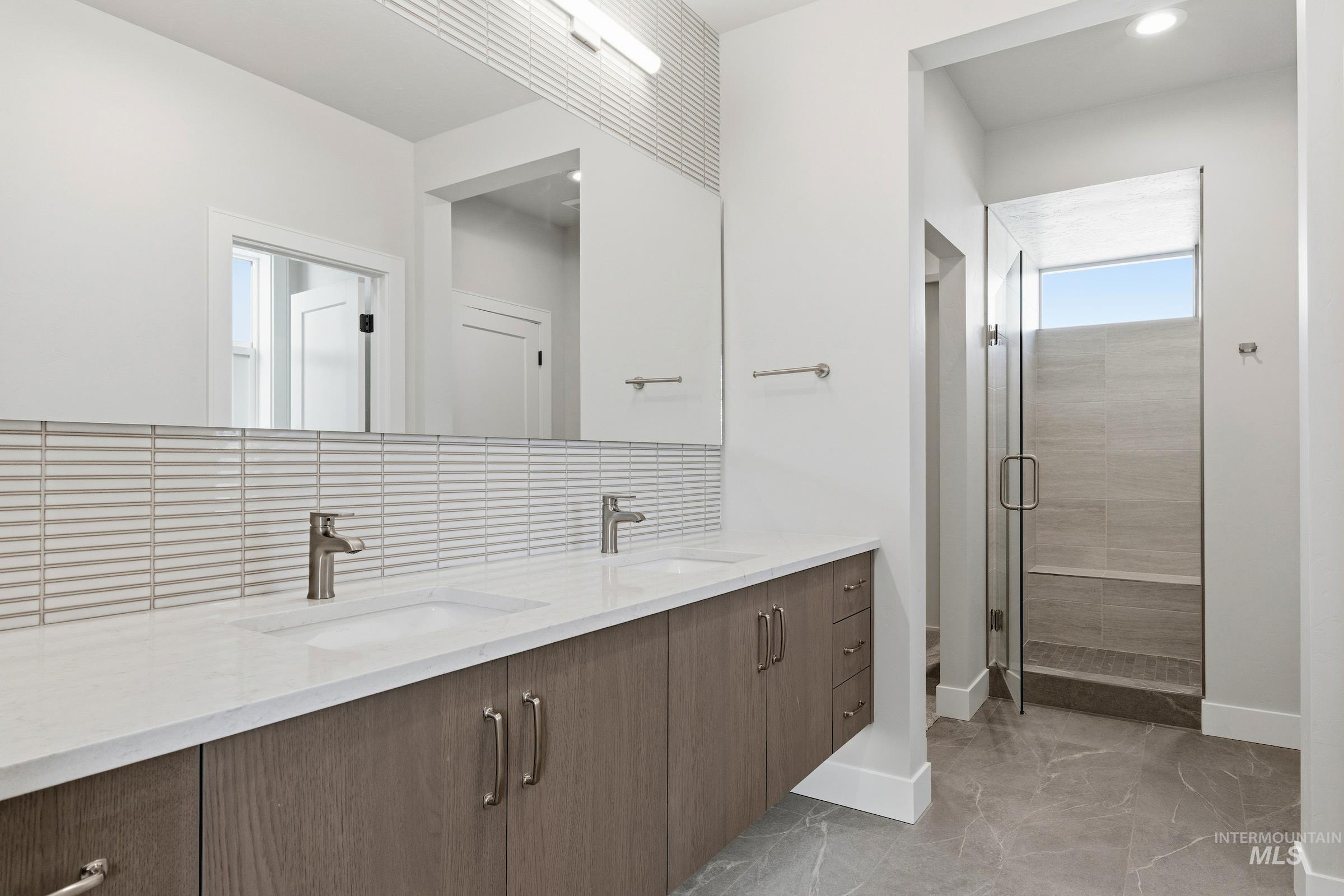 Full bath with double vanity, a shower stall, decorative backsplash, and light marble finish floors
