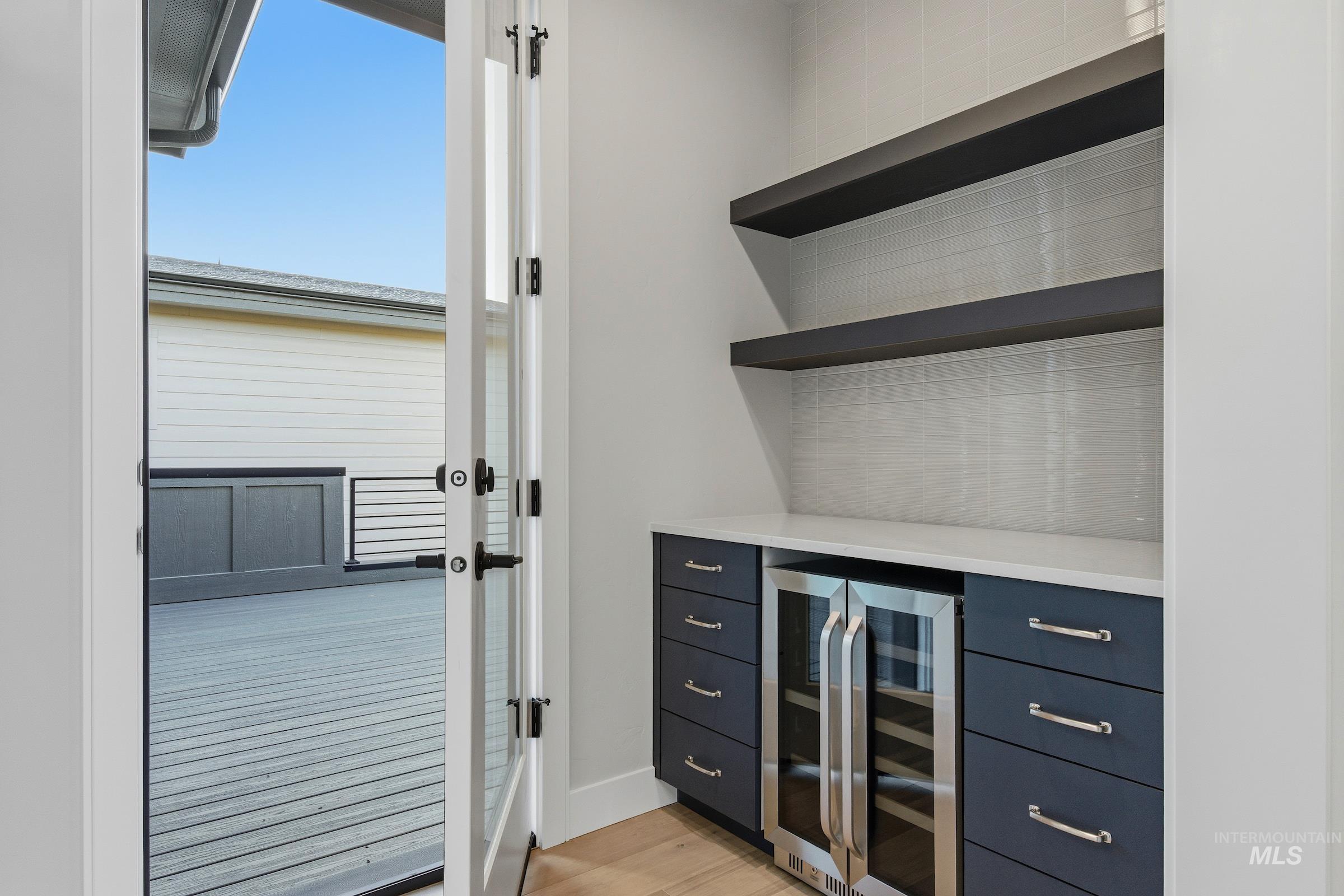 Bar featuring wine cooler, light wood-type flooring, light stone countertops, decorative backsplash, and open shelves