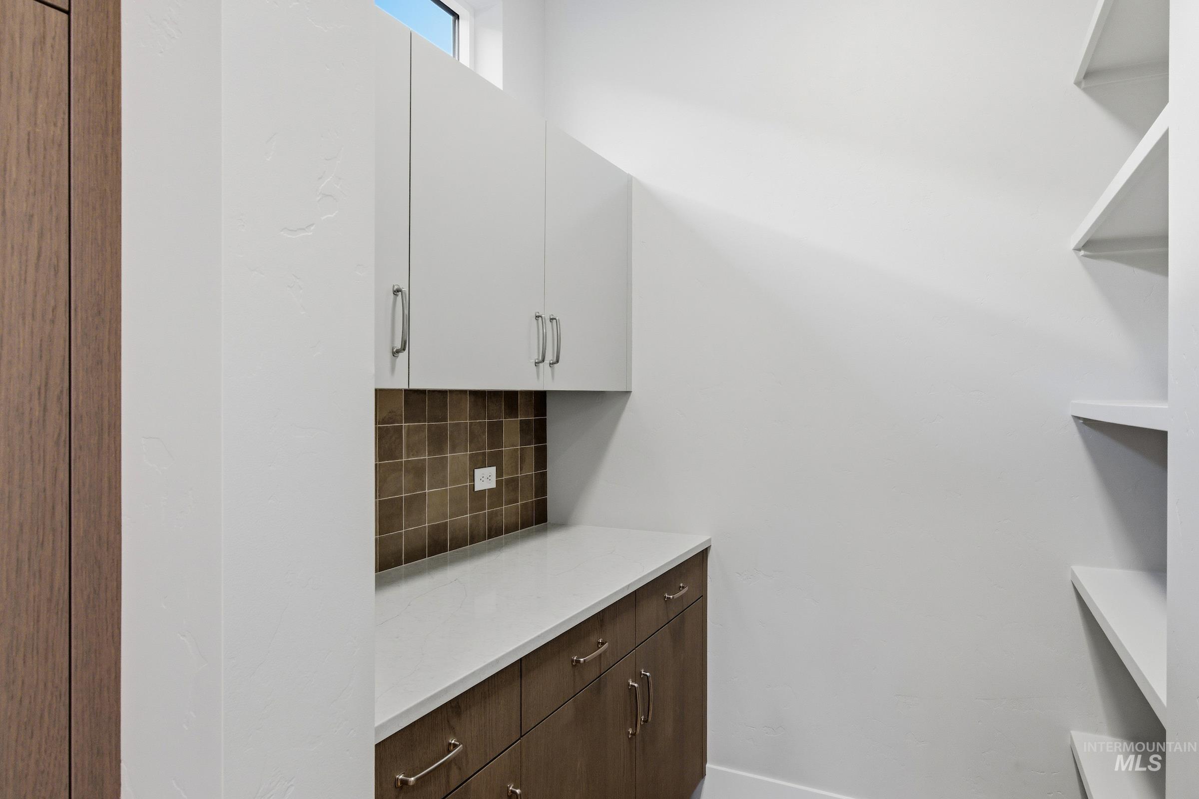 Bar area with dark brown cabinets, decorative backsplash, white cabinetry, light stone countertops, and modern cabinets