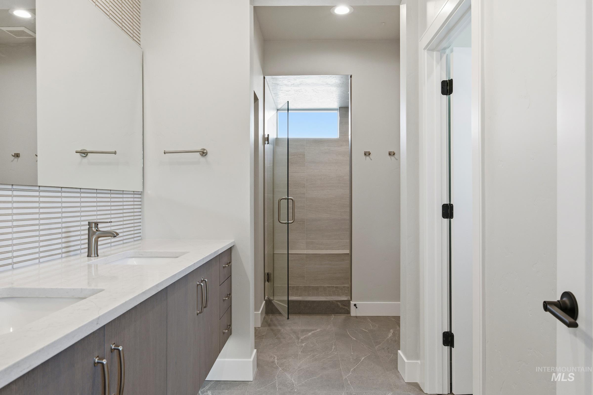Bathroom with double vanity, a shower stall, recessed lighting, and decorative backsplash