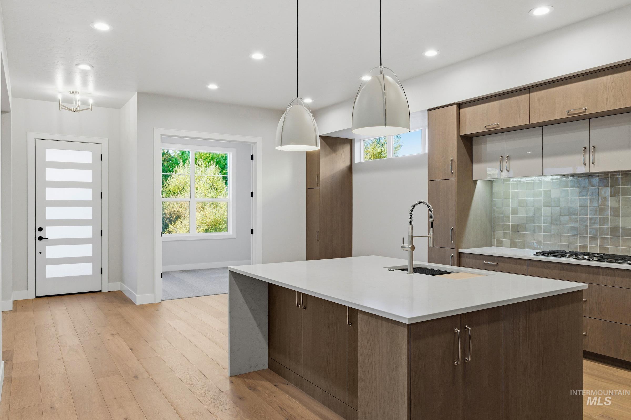 Kitchen with backsplash, healthy amount of natural light, light stone countertops, recessed lighting, and light wood finished floors
