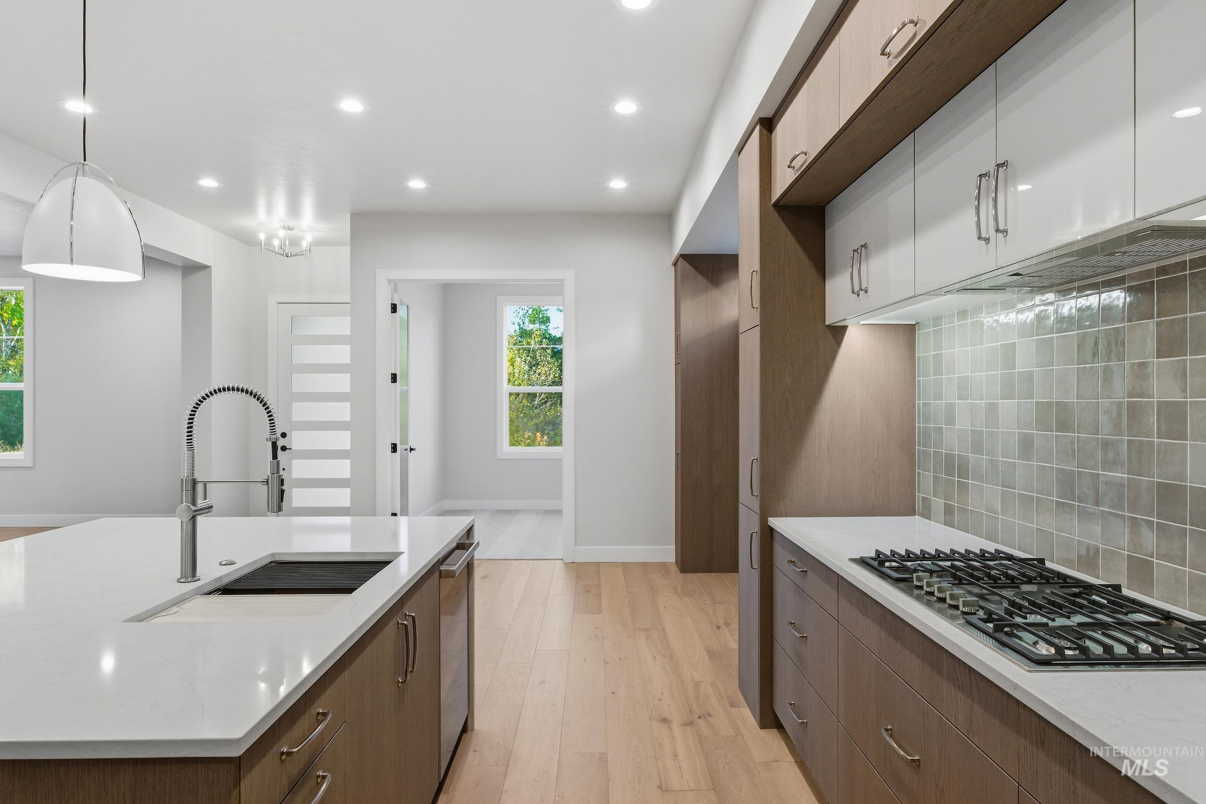 Kitchen featuring modern cabinets, decorative backsplash, light wood-type flooring, stainless steel appliances, and recessed lighting