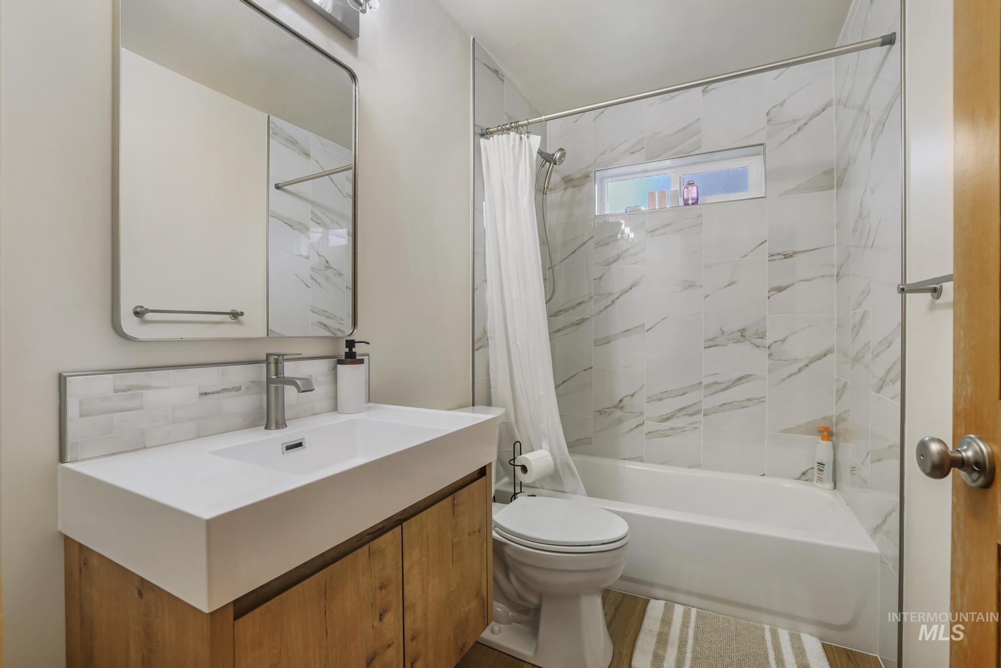 Full bath with shower / bath combination with curtain, vanity, and tasteful backsplash