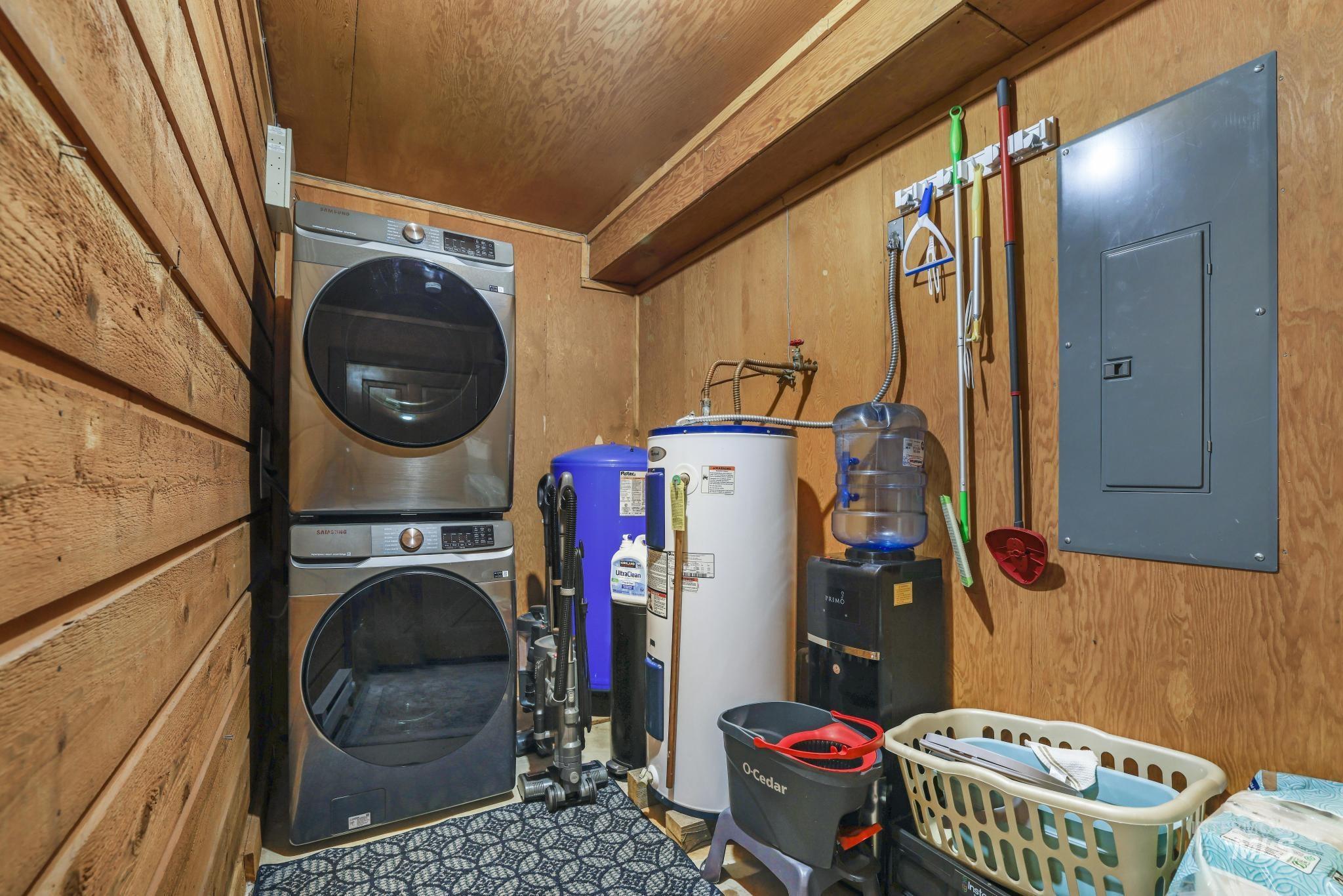 Washroom featuring wooden walls, electric panel, electric water heater, stacked washer and clothes dryer, and wood ceiling