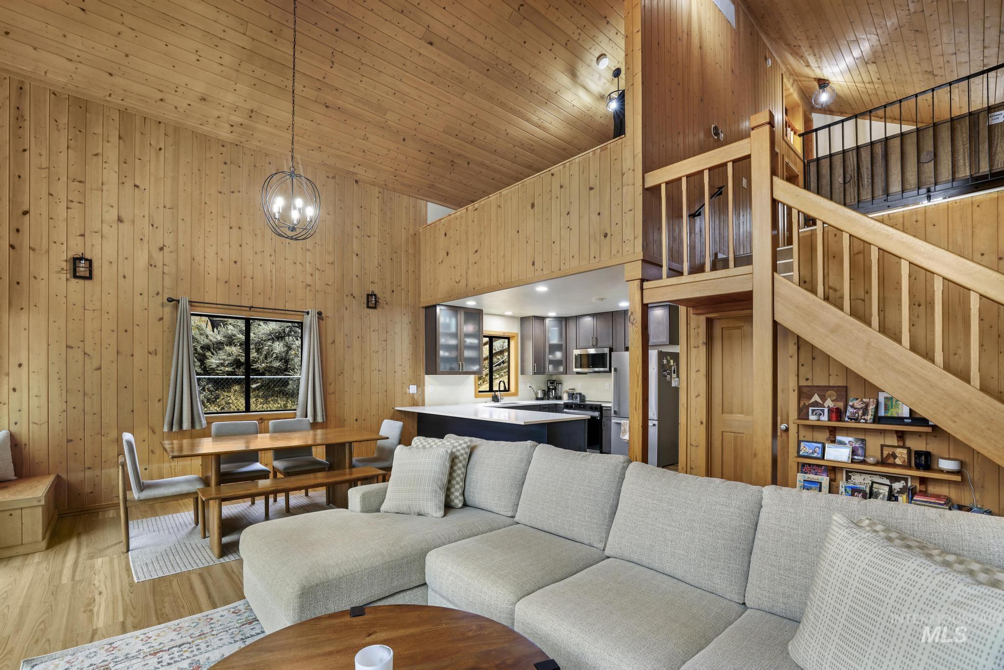 Living area with wooden walls, a towering ceiling, wood finished floors, wooden ceiling, and a chandelier