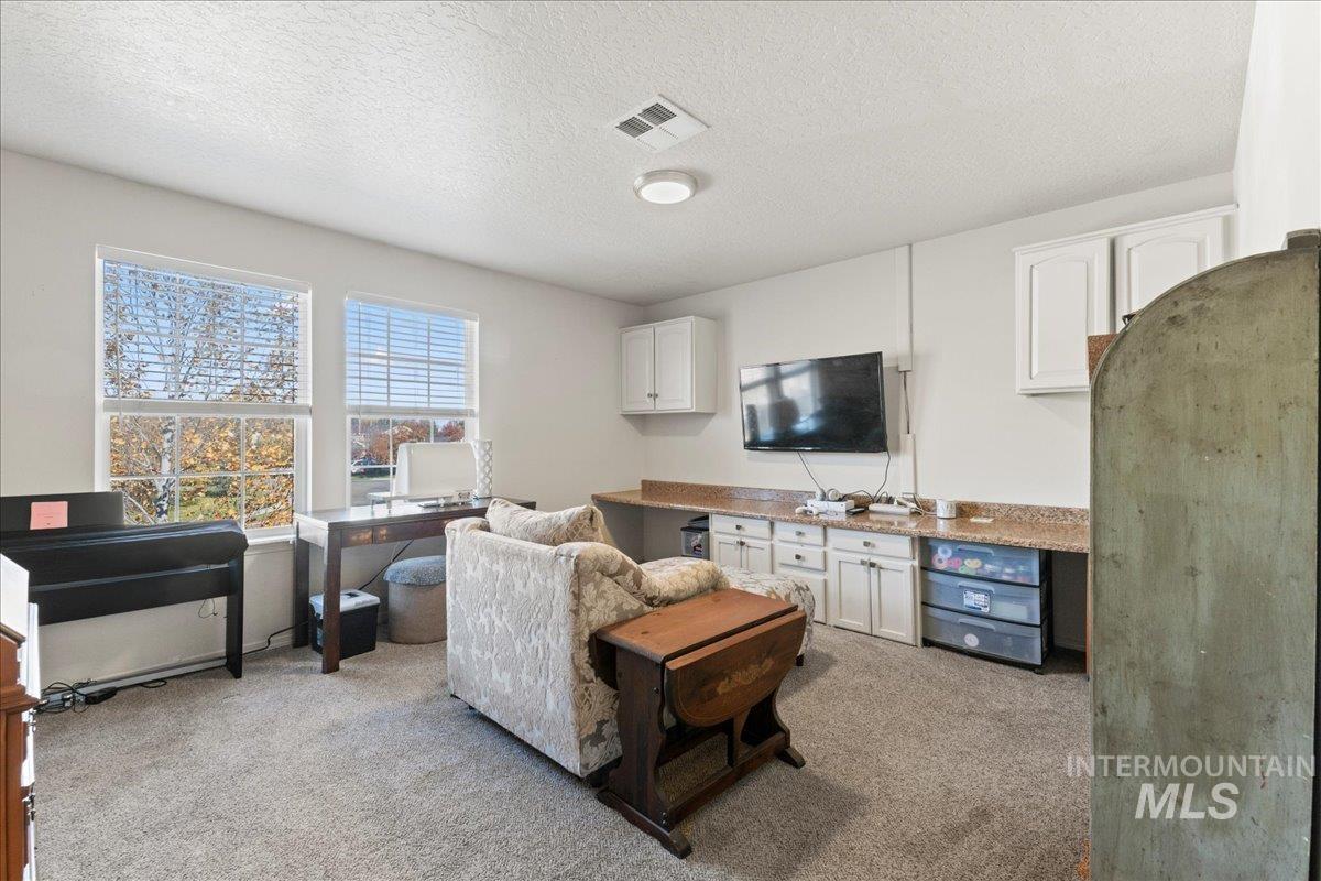Living room featuring light colored carpet, a textured ceiling, and a desk