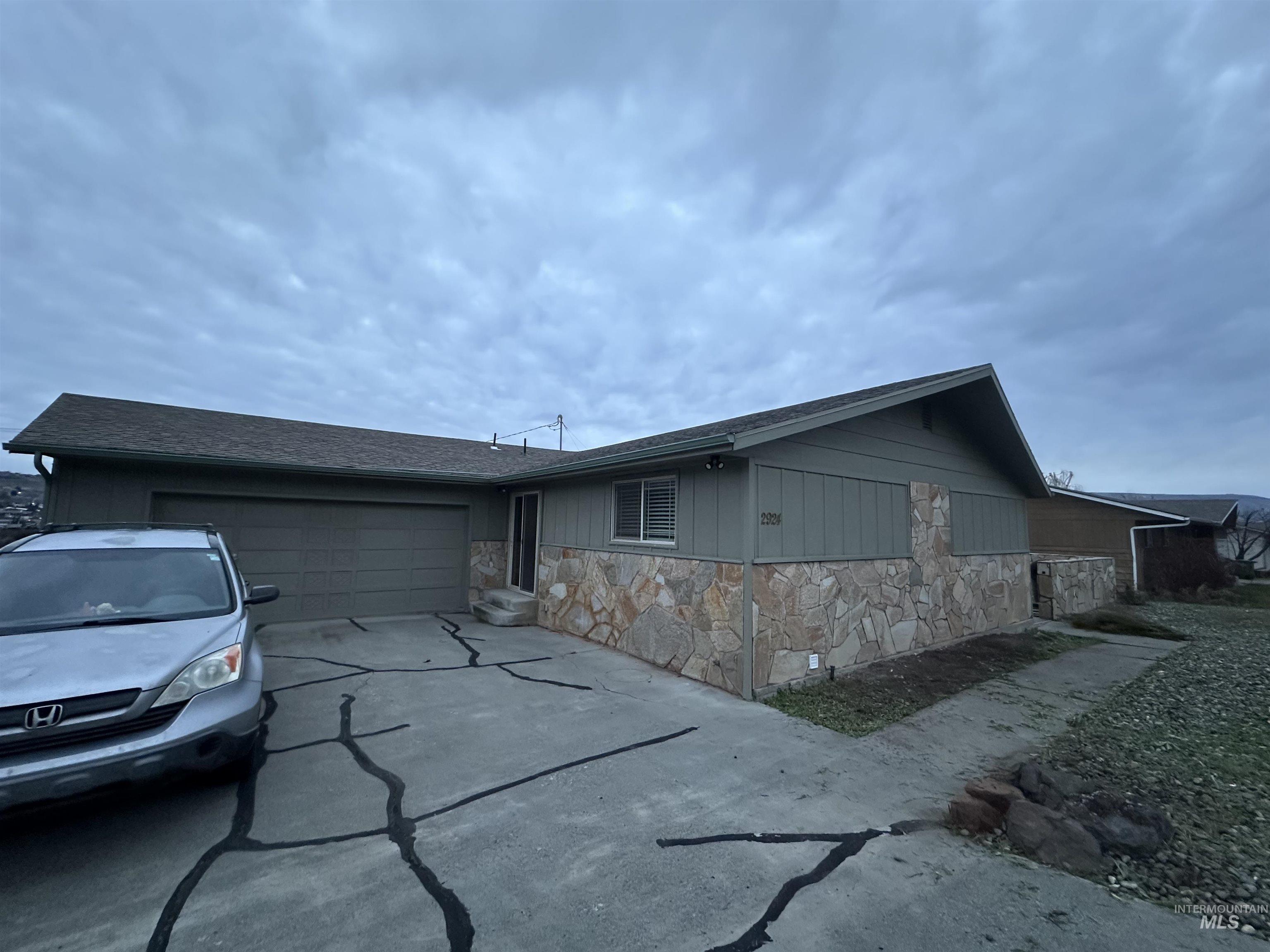Ranch-style house featuring stone siding, concrete driveway, an attached garage, and a shingled roof