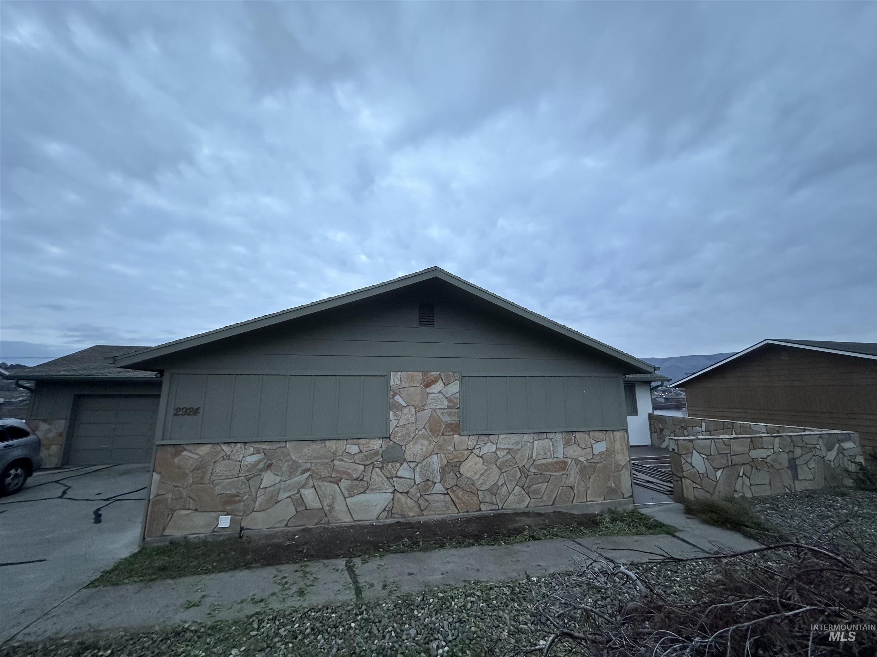View of side of home with stone siding, an attached garage, and driveway