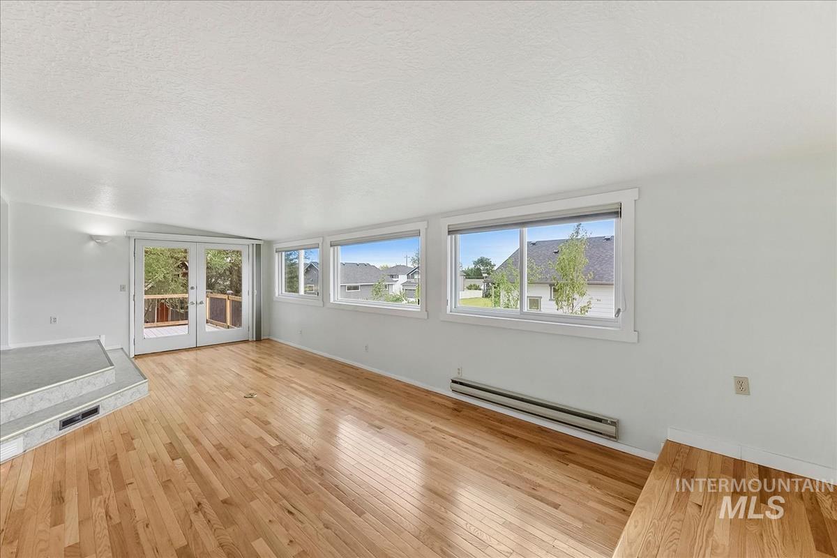 Spacious living area featuring light wood-finish flooring, multiple large windows, and white walls