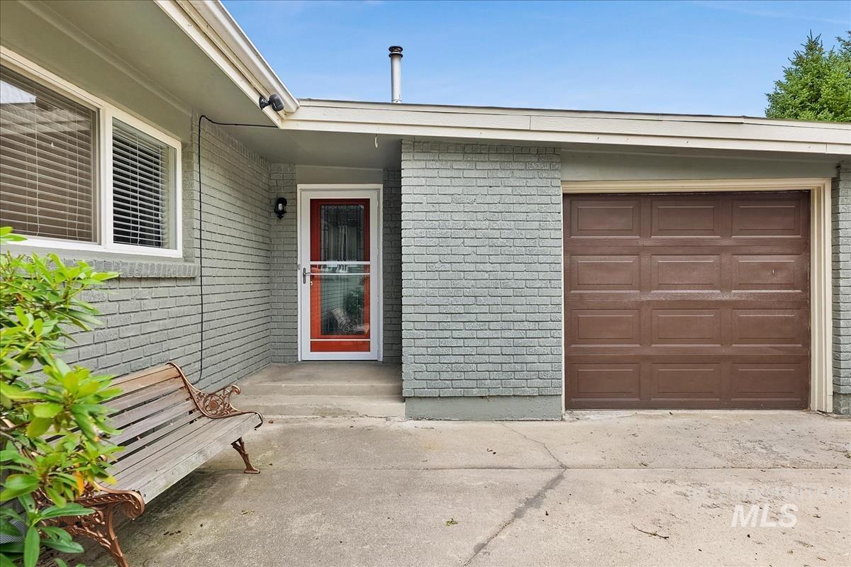 Exterior featuring gray brick siding, a paneled brown garage door, and a red entry door with a storm door