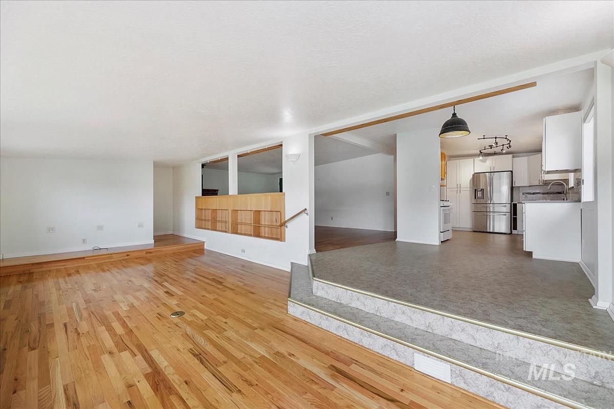 Multi-level interior featuring hardwood flooring, a built-in wood display shelf with interior windows, a kitchen with white cabinetry, stainless steel appliances, and a pendant light fixture