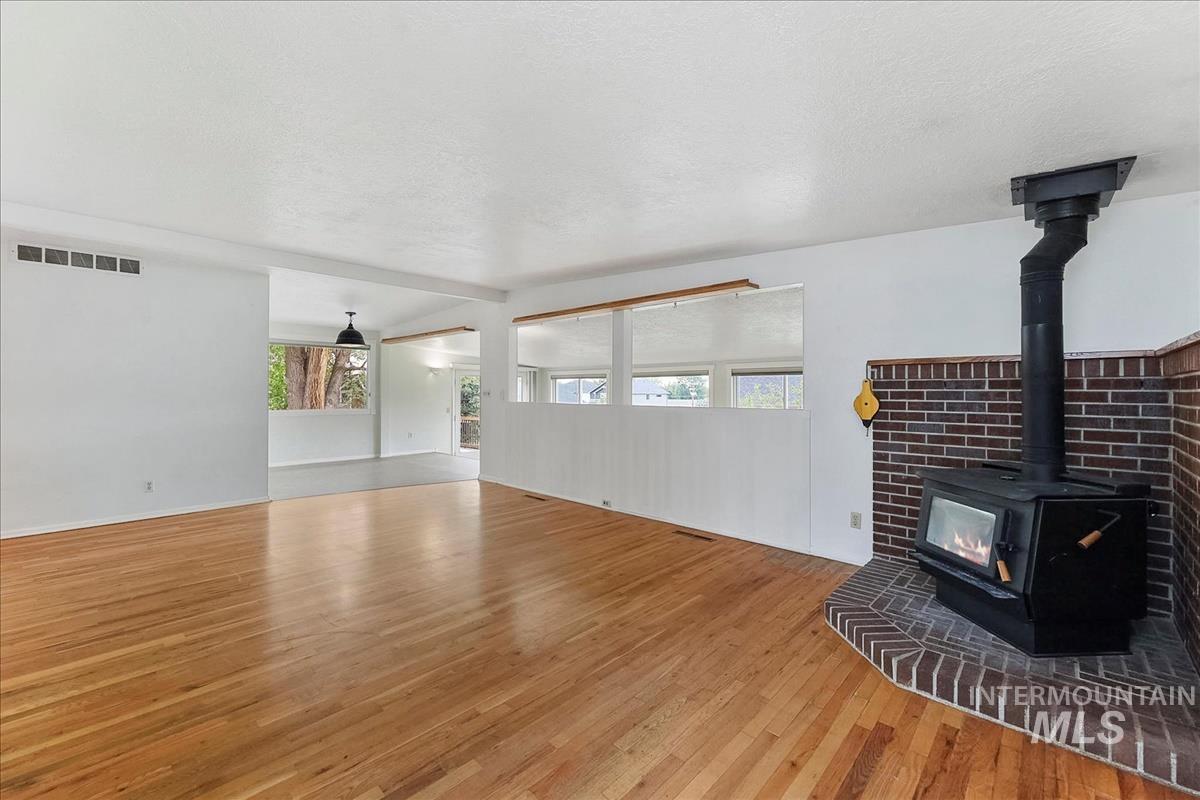Hardwood flooring spanning the open-concept room, featuring a corner wood-burning stove with a brick surround and hearth
