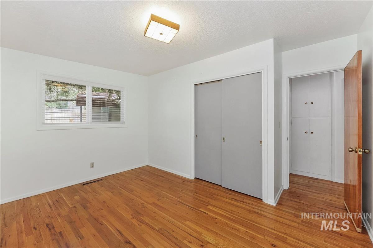Room featuring wood flooring, white walls, and a window with blinds