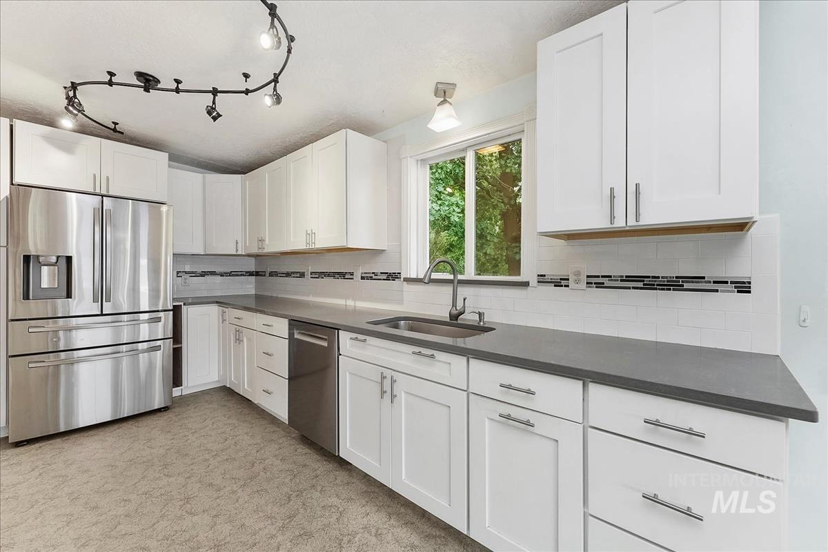 Modern kitchen featuring stainless steel appliances, white shaker-style cabinetry, dark countertops, a subway tile backsplash with decorative accents, and track lighting