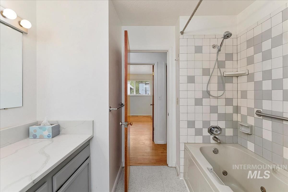 Bathroom featuring a built-in tub with shower, checkerboard wall tiling, and a vanity with a white countertop