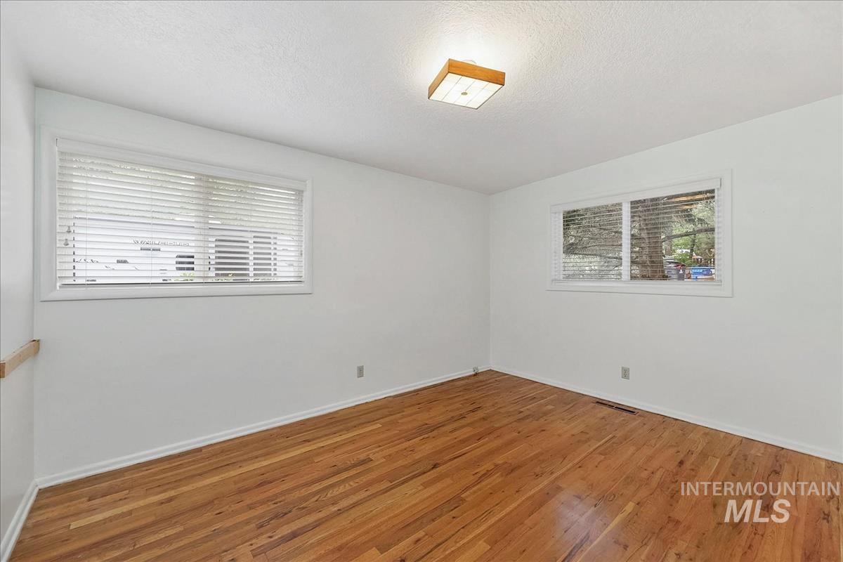 Room featuring wood-finish flooring, white walls, and two windows with blinds