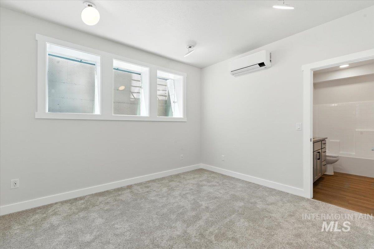 Unfurnished bedroom featuring a wall mounted air conditioner, carpet flooring, and ensuite bath