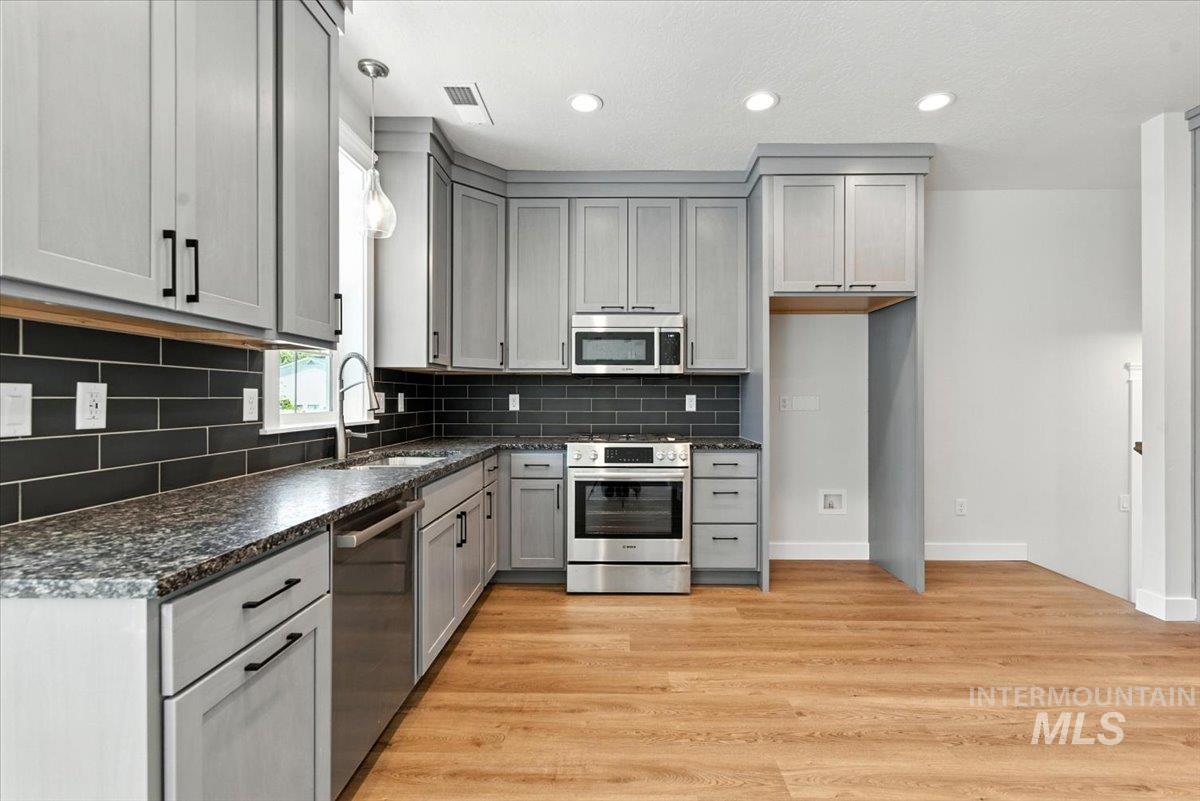 Kitchen with stainless steel appliances, gray cabinetry, backsplash, recessed lighting, and light wood-style floors