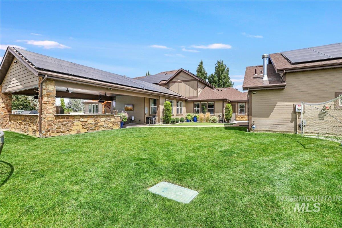 Back of property with solar panels, a ceiling fan, a lawn, and stone siding