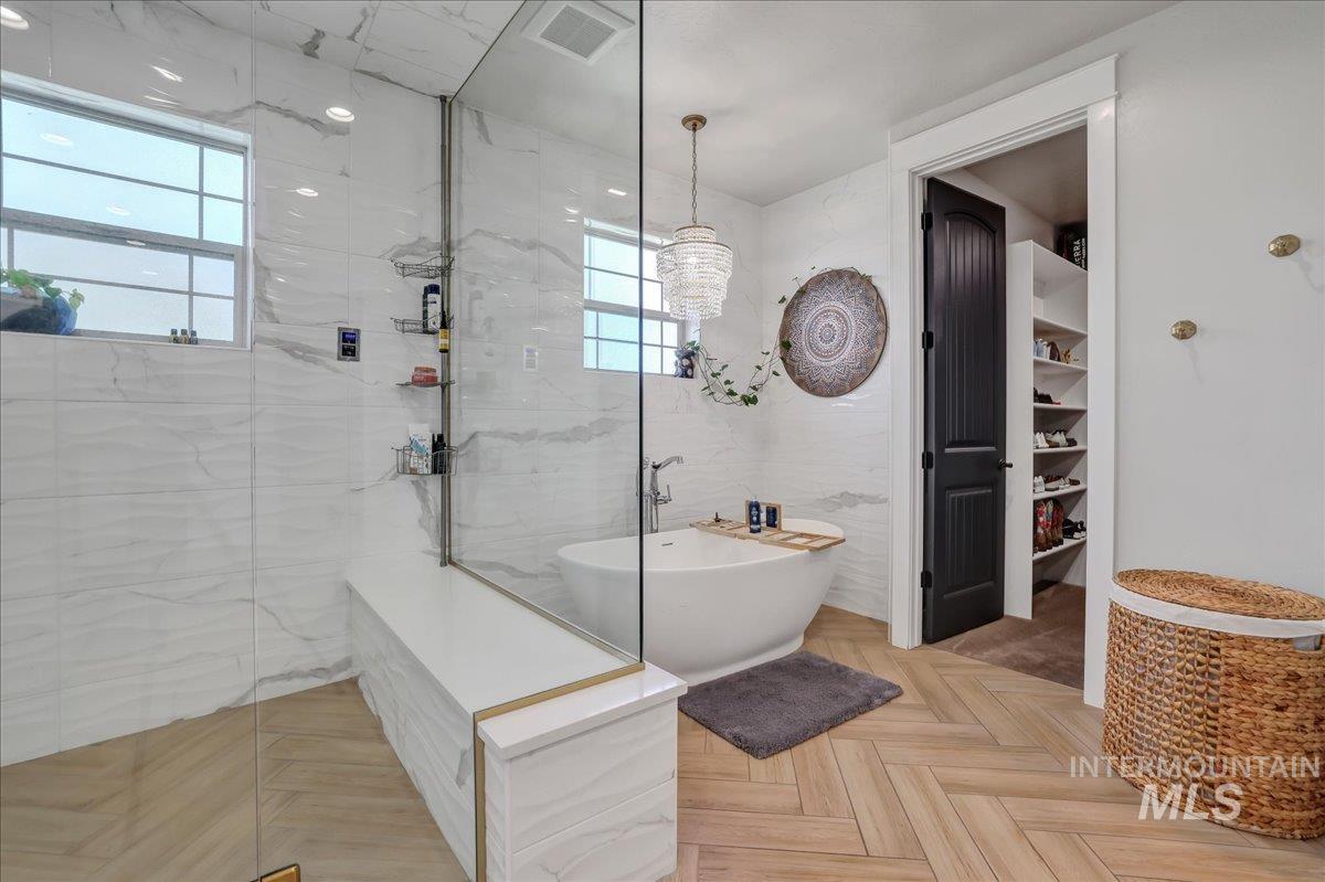 Full bath featuring a marble finish shower, a soaking tub, a chandelier, and tile walls