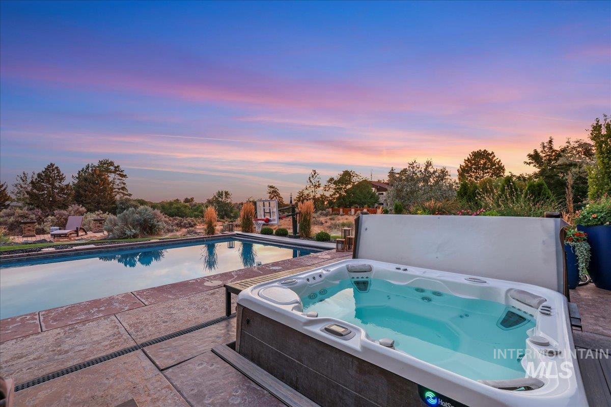 Pool at dusk with a hot tub and a patio area