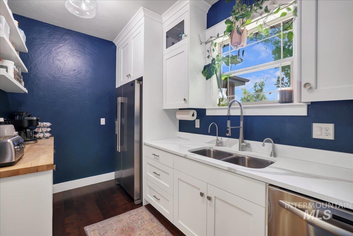 Kitchen with appliances with stainless steel finishes, butcher block counters, dark wood finished floors, white cabinetry, and a textured wall