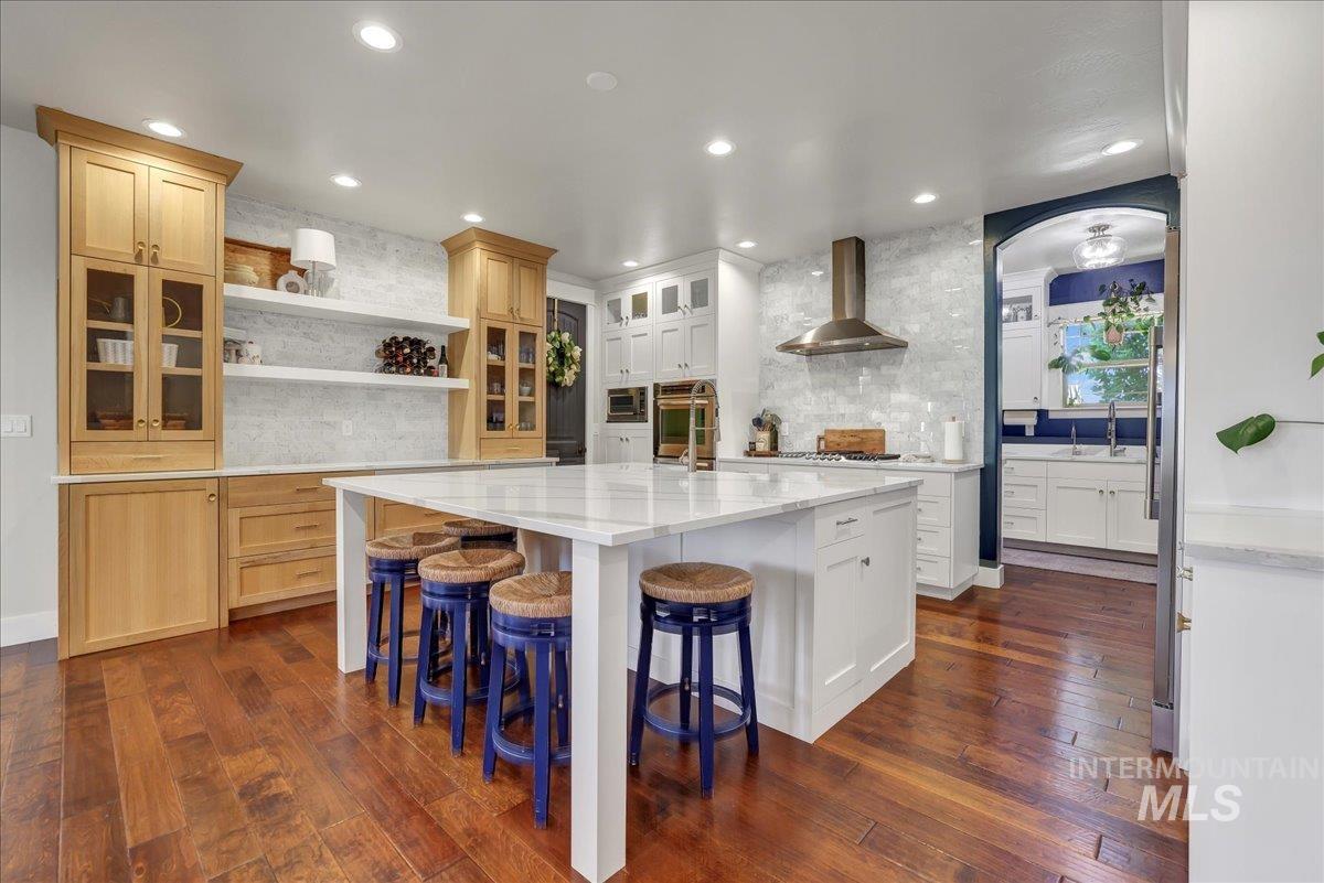 Kitchen featuring backsplash, an island with sink, dark wood-style flooring, recessed lighting, and a breakfast bar area