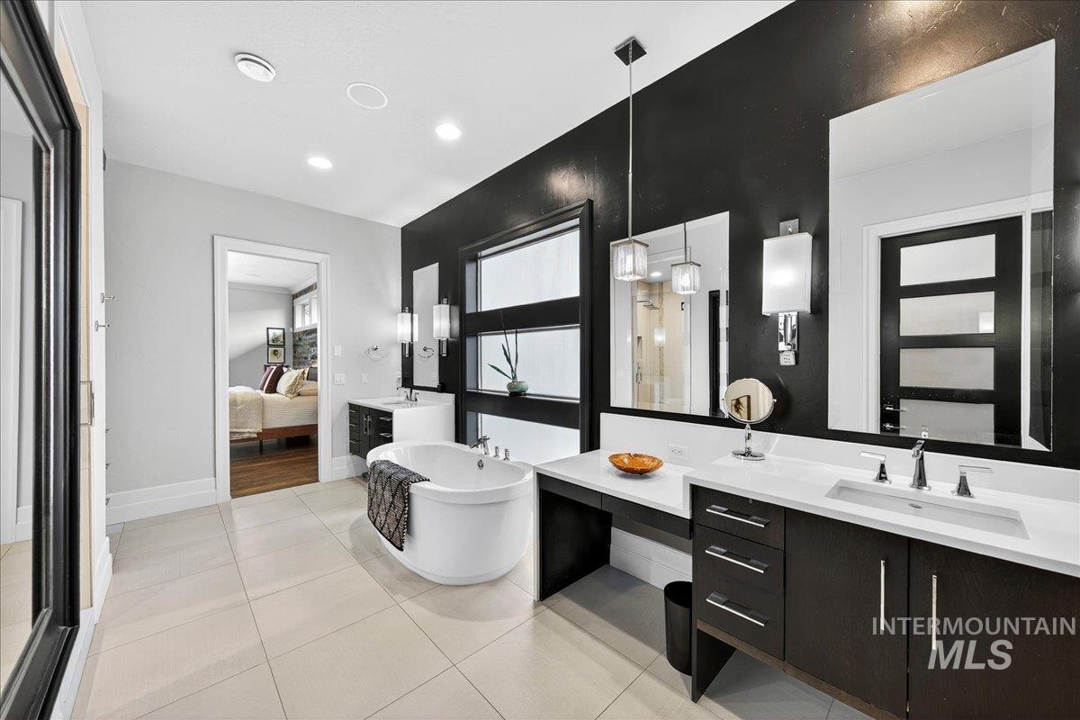 Ensuite bathroom with a freestanding tub, two vanities, light tile patterned floors, and recessed lighting