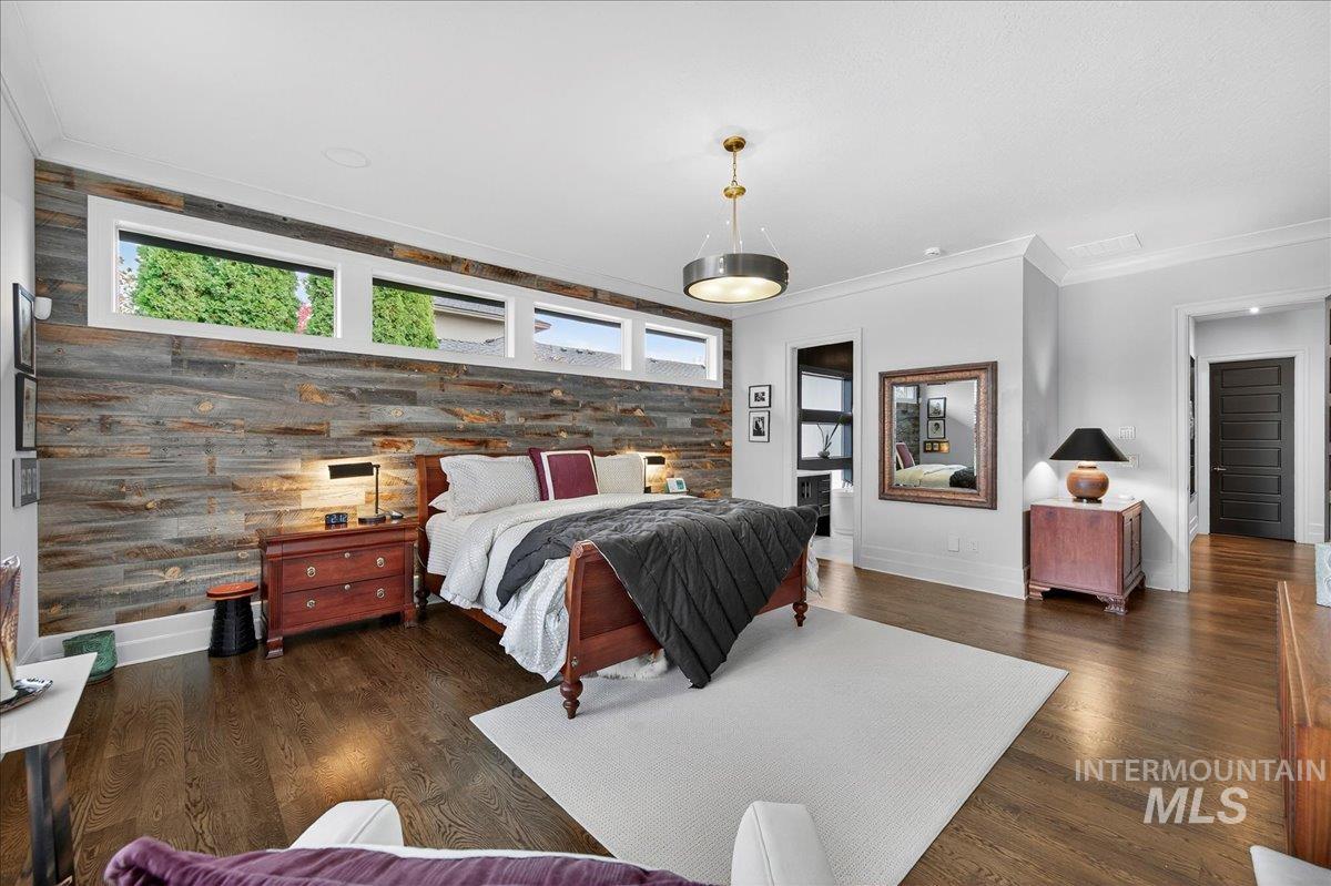 Bedroom with an accent wall, crown molding, dark wood finished floors, and multiple windows