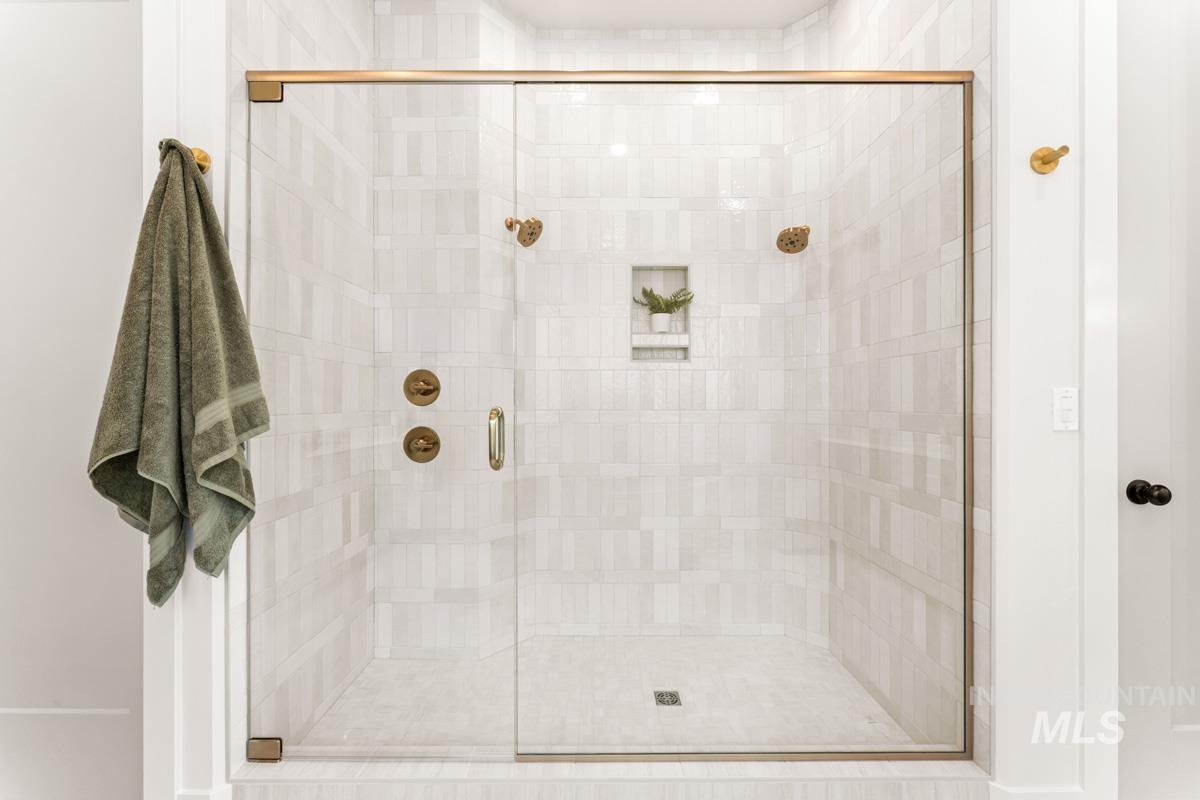 Glass-enclosed shower featuring light-toned rectangular tile walls and floor, a built-in shower niche, and brass-finish fixtures