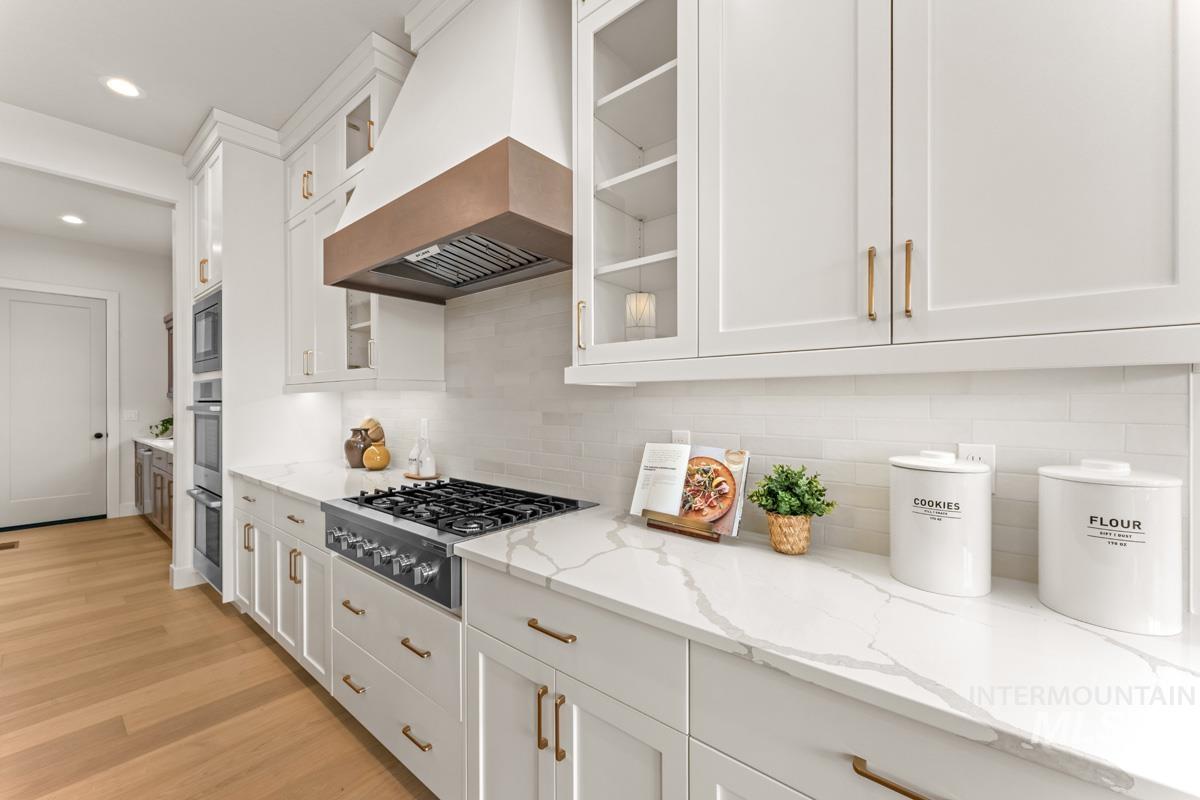 Gourmet kitchen featuring a built-in range, white shaker cabinetry, quartz countertops, a subway tile backsplash, and wood-finish flooring