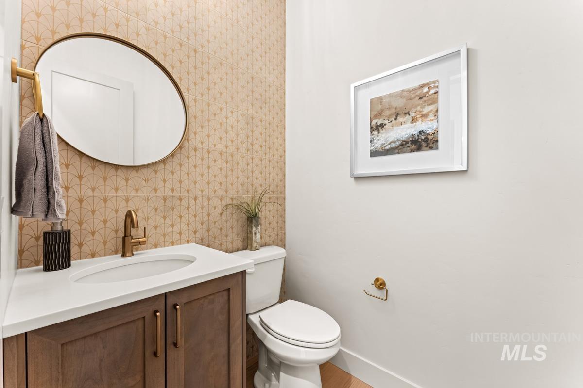 Bathroom featuring a patterned accent wall, a vanity with a white countertop and wood-finish cabinetry, and brass-finish fixtures