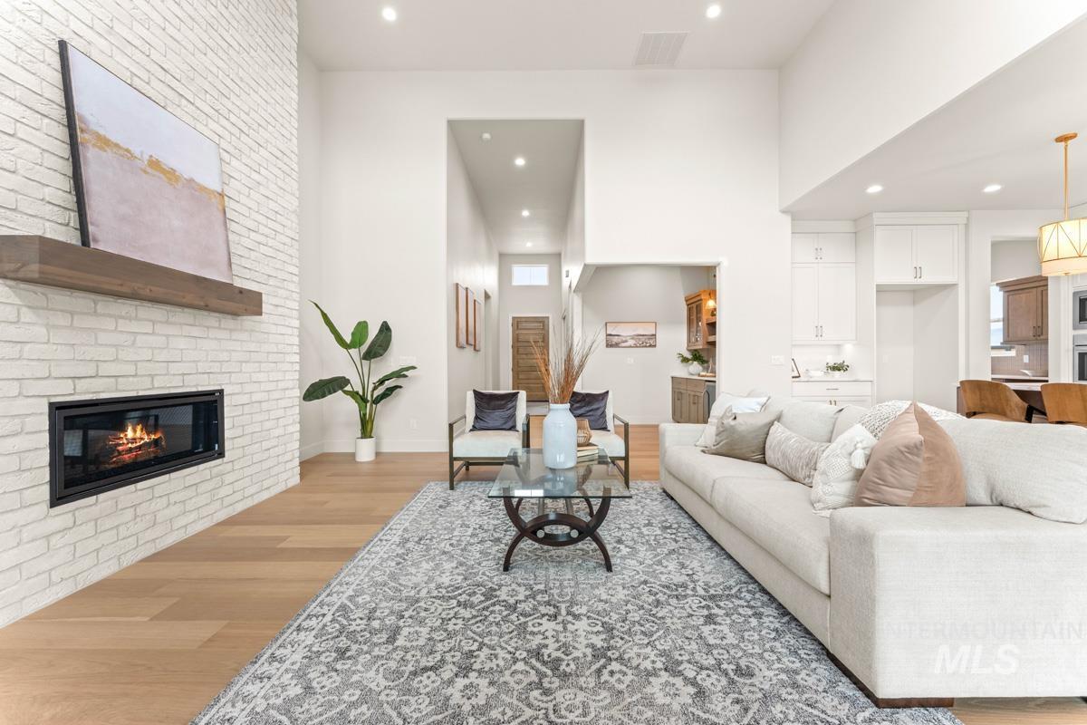 Spacious living area featuring a tall, painted brick fireplace with a wood mantel, wood-finish flooring, recessed lighting, and a brightly lit open concept