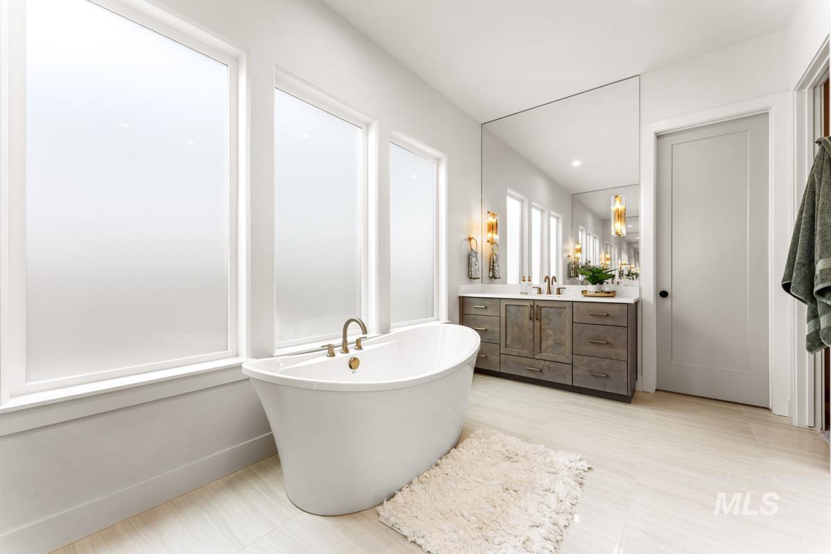 Freestanding soaking tub with brass fixtures, illuminated by multiple tall frosted-glass windows