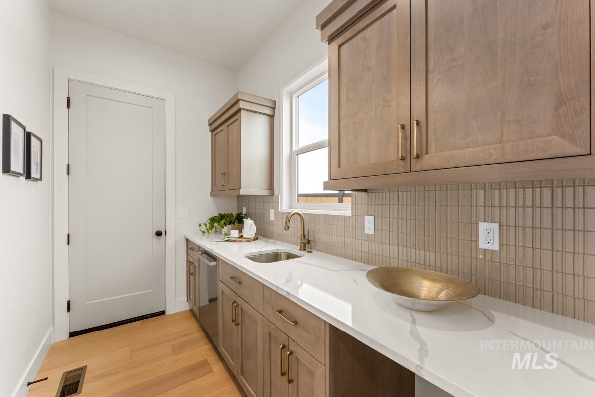 Kitchenette featuring light wood-finish cabinetry, white marble-look countertops, and a vertical subway tile backsplash