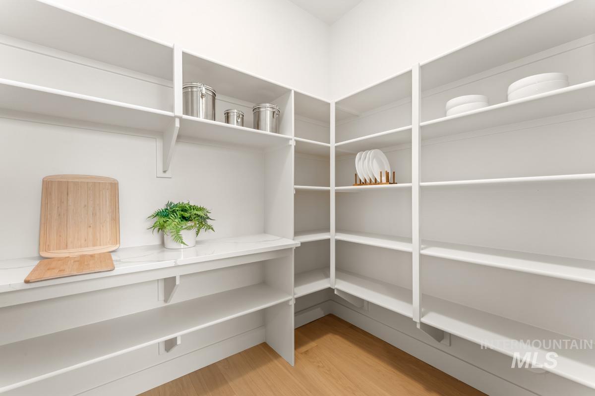 Spacious corner pantry featuring extensive built-in shelving, a marble-finish countertop, and wood-finish flooring