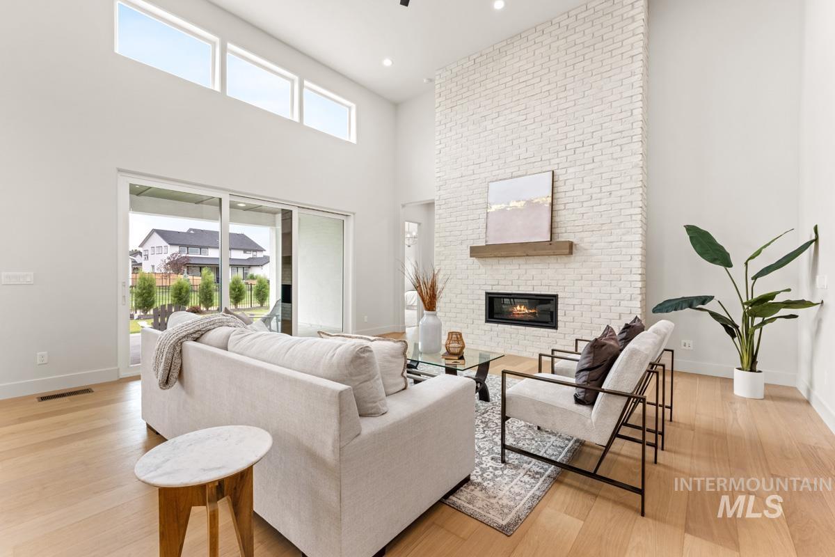 Two-story living area featuring a white brick fireplace with a wood mantle, an integrated linear fireplace, and wood-finish flooring