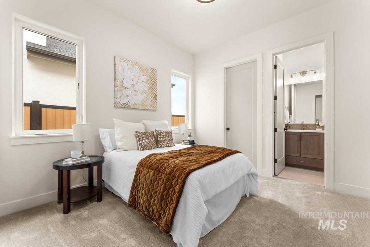 Carpeted bedroom with white walls and trim, two windows, and an en-suite bathroom featuring a vanity with a light-colored countertop
