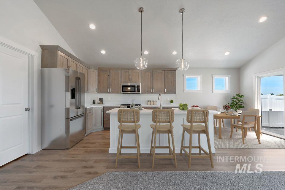Kitchen with stainless steel appliances, lofted ceiling, light countertops, backsplash, and light wood-style floors