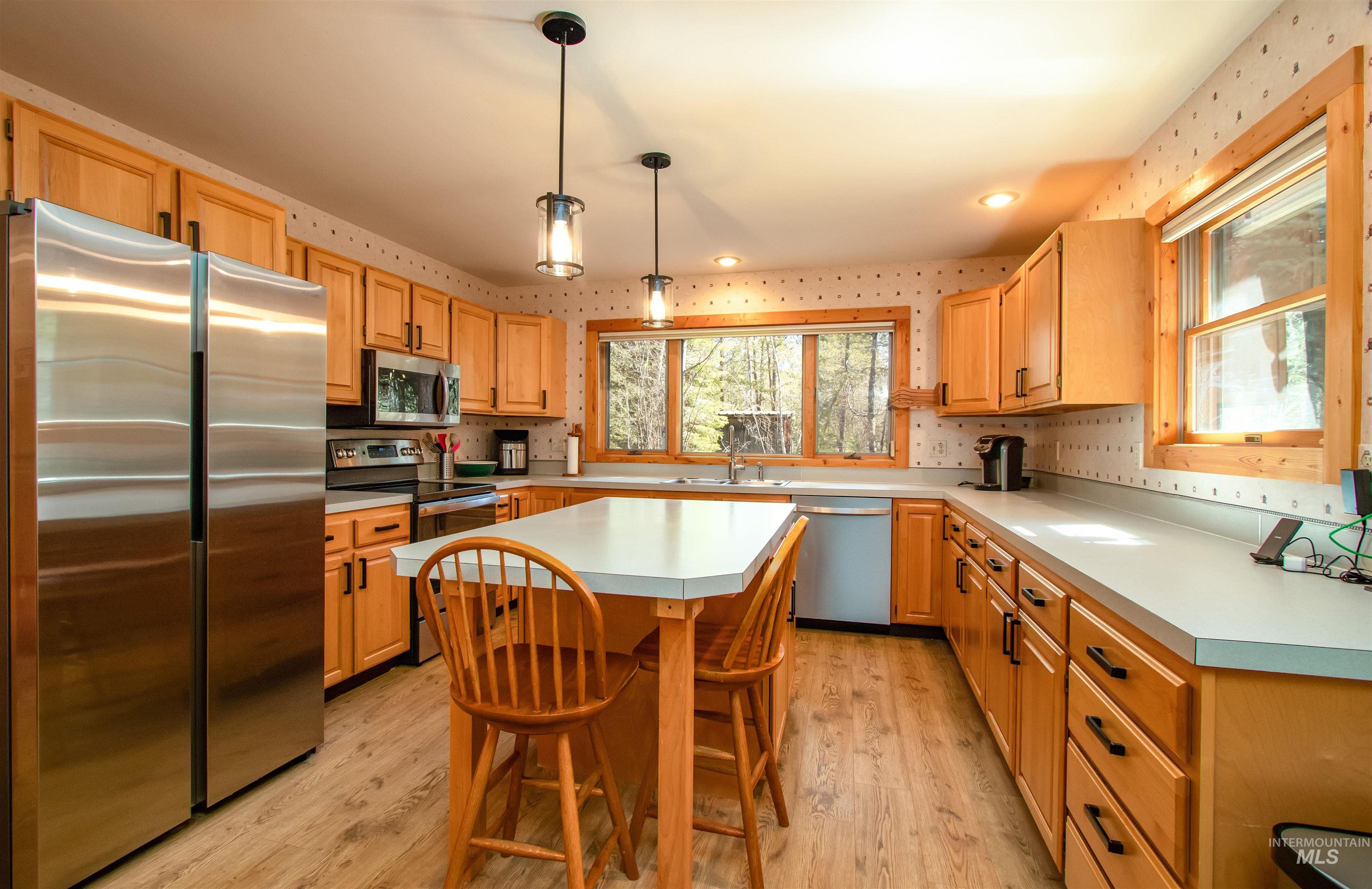 Kitchen with stainless steel appliances, light countertops, light wood-style flooring, a kitchen breakfast bar, and wallpapered walls