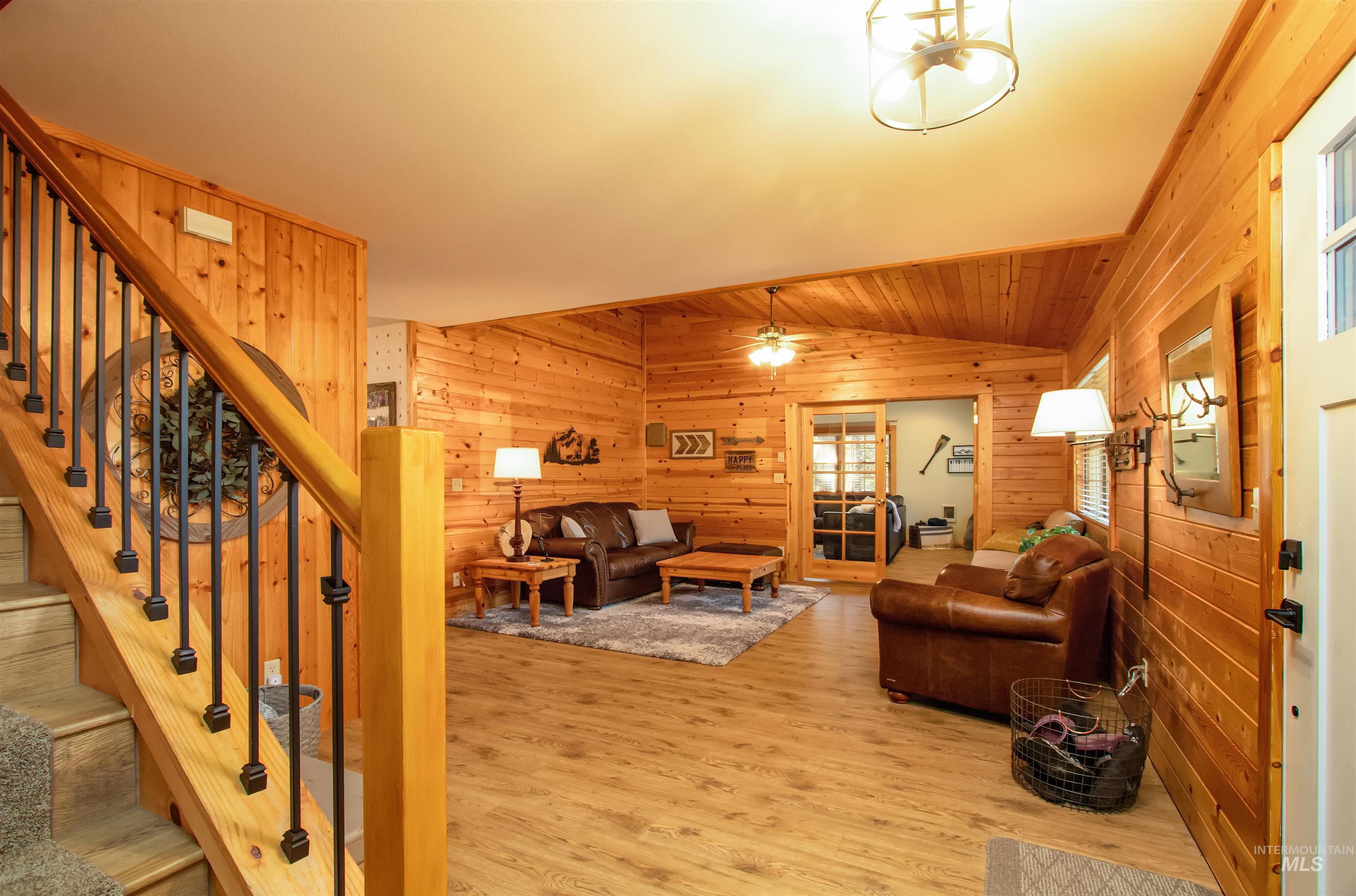 Living room featuring lofted ceiling, wood walls, wood finished floors, and a ceiling fan