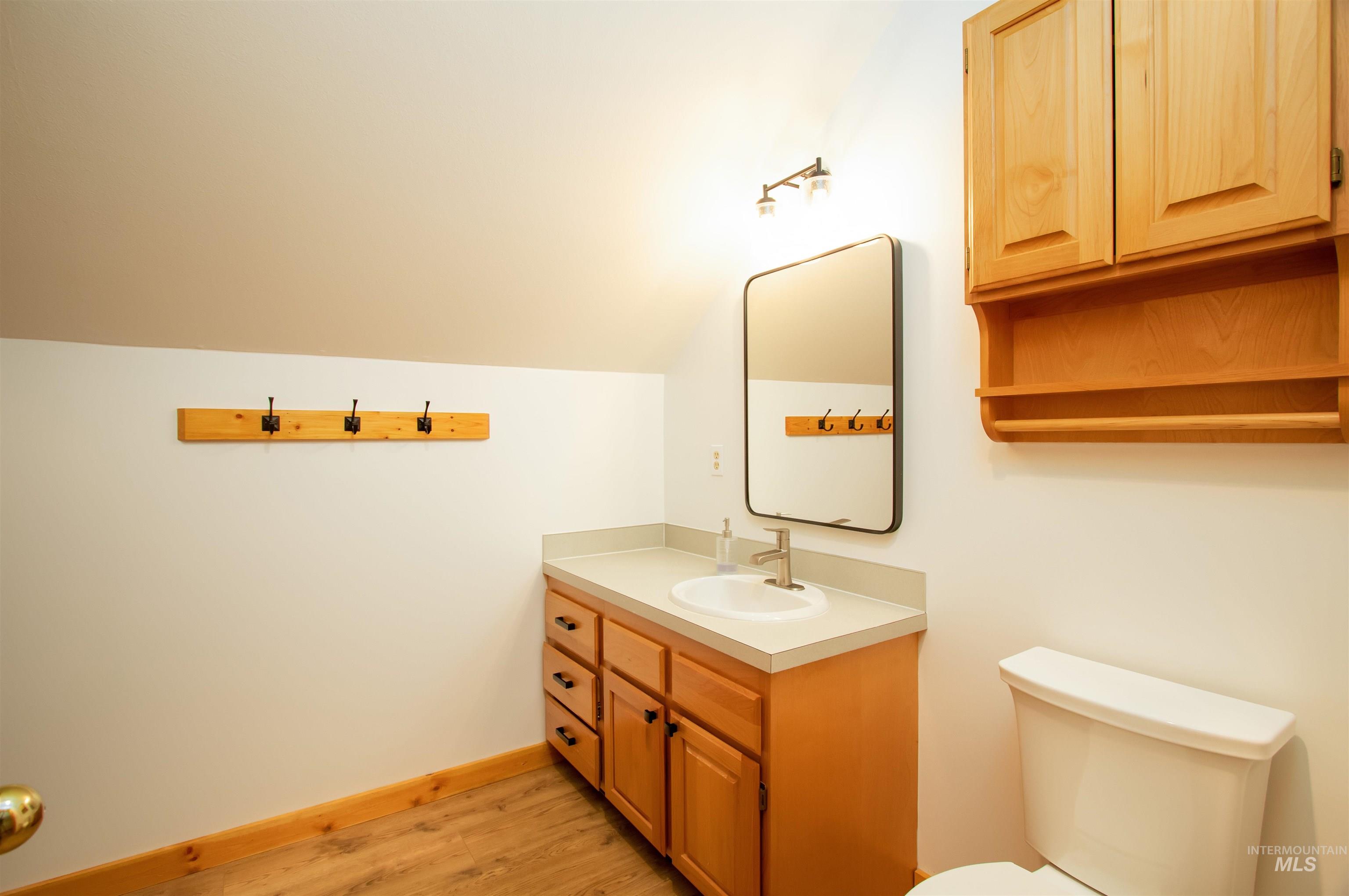 Half bathroom with vanity, vaulted ceiling, and light wood-style floors