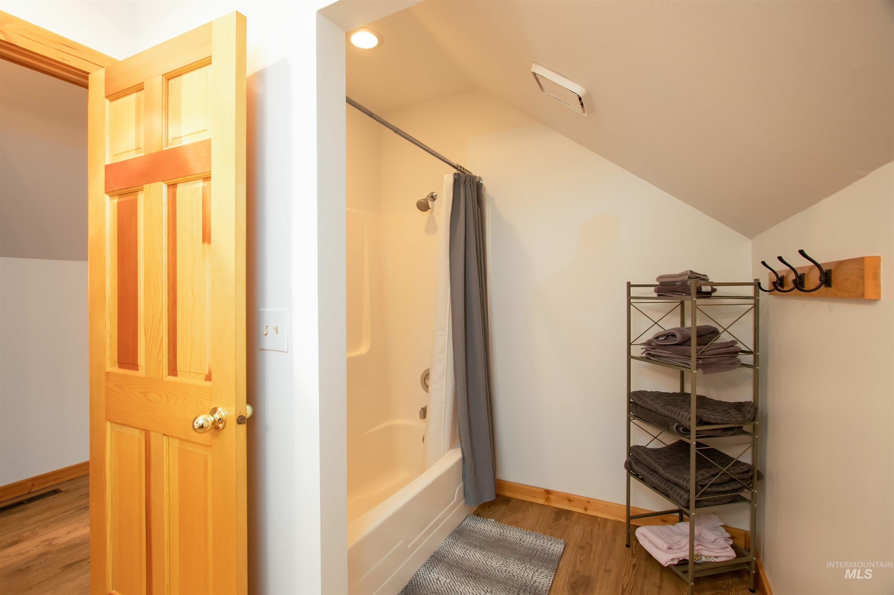 Full bath with lofted ceiling, light wood-type flooring, and shower / bath combo