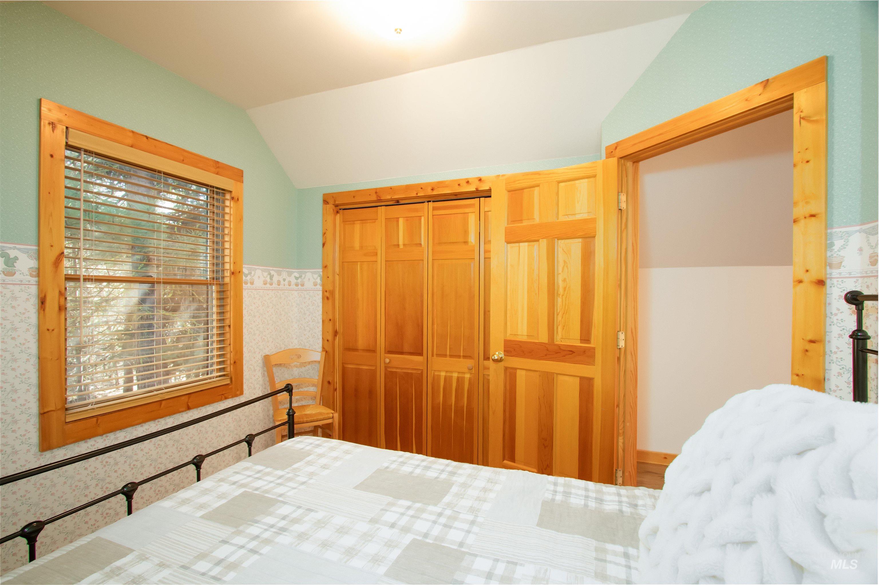 Bedroom with wallpapered walls, a wainscoted wall, a closet, and lofted ceiling