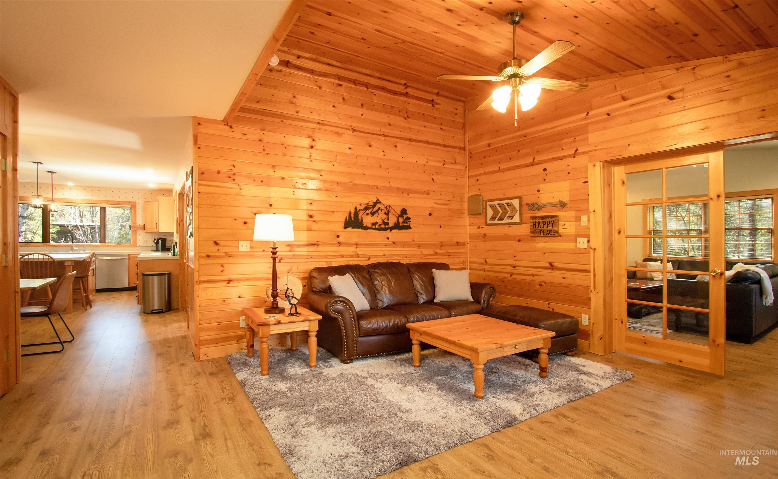 Living room featuring light wood-style flooring, wooden walls, and ceiling fan
