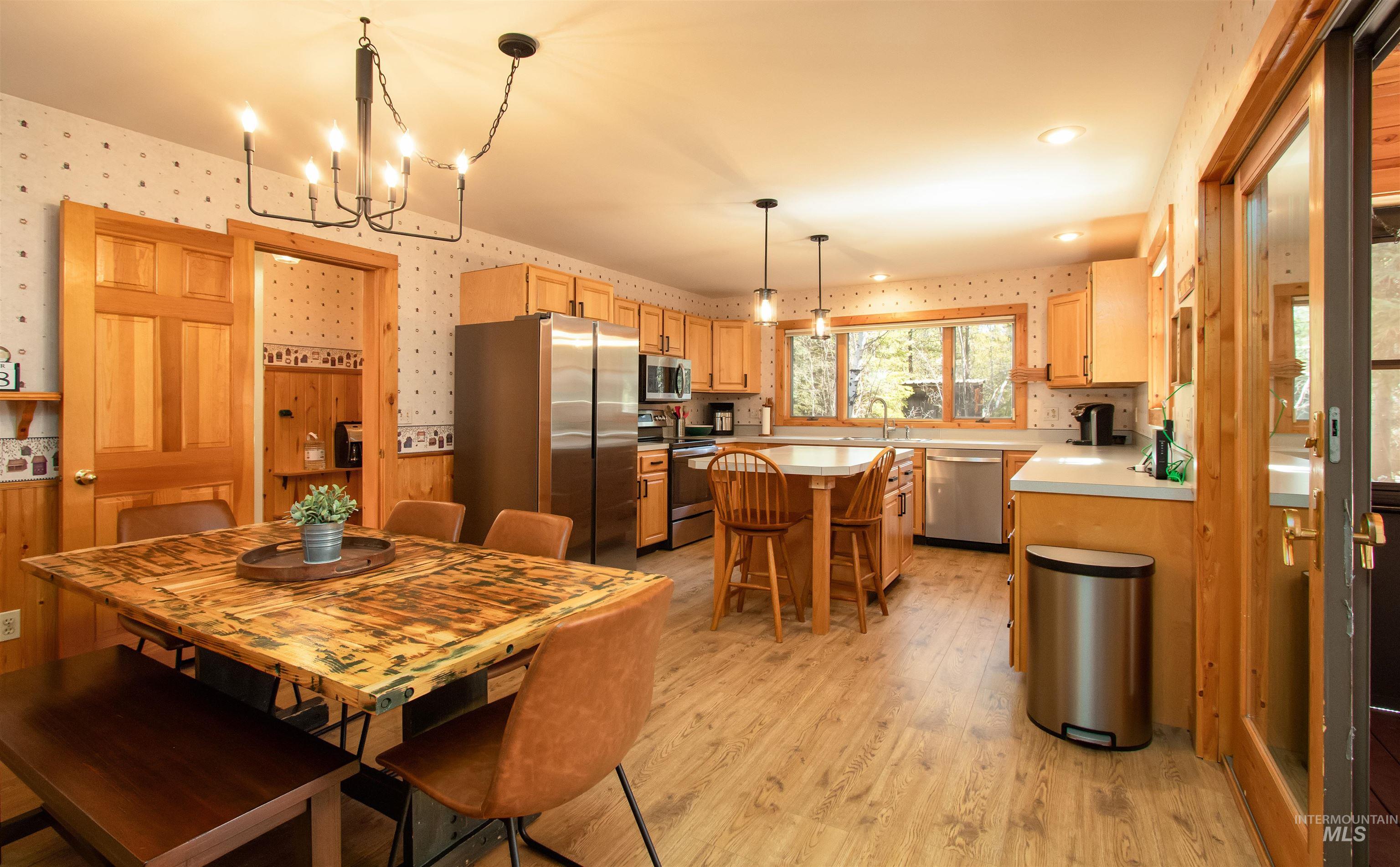 Dining area featuring wallpapered walls, light wood-style floors, hanging lights, and wainscoting
